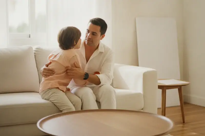 הורה וילד יושבים יחד על ספה בסלון מואר ומשוחחים בשקט, ממחיש סרבנות קשר וניכור הורי