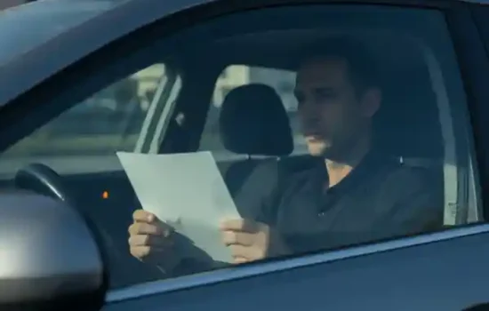 נהג יושב ברכב חונה ובוחן מסמך באור בוקר