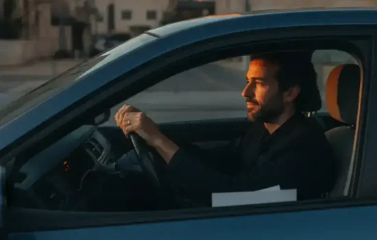 נהג יושב ברכב חונה בשעת זהב ומחזיק את ההגה, מביט קדימה בריכוז, על רקע דוח אי שמירת מרחק