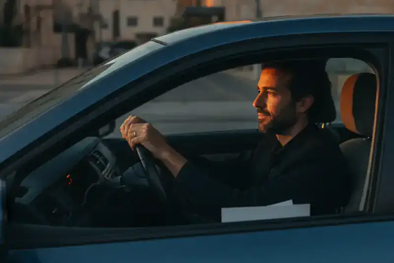 נהג יושב ברכב חונה בשעת זהב ומחזיק את ההגה, מביט קדימה בריכוז, על רקע דוח אי שמירת מרחק