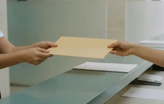 תיקייה סגורה נמסרת בין שתי ידיים מעל דלפק