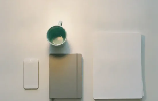 מבט מלמעלה על שולחן משרדי ריק בערב עם מנורה חמה, טלפון הפוך ומחברת סגורה, המחשה לפיקוח מעסיק על עובדים